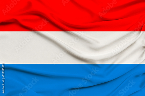 beautiful photo of the Luxembourg national flag on delicate shiny silk with soft draperies, the concept of state power, country life, horizontal, close-up, copy space