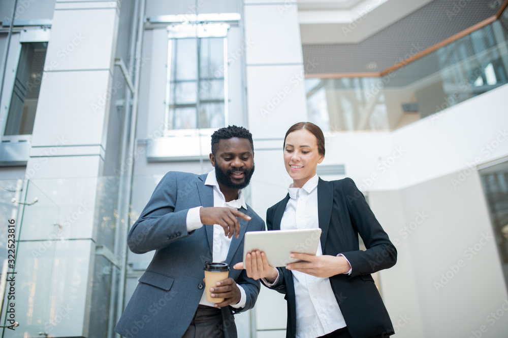 Positive Black manager with coffee cup pointing at tablet while discussing sales plan with colleague Positive Black manager with coffee cup pointing at tablet while discussing sales plan with colleague