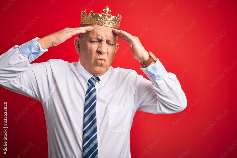 Senior handsome businessman wearing king crown standing over isolated red background suffering from headache desperate and stressed because pain and migraine. Hands on head.