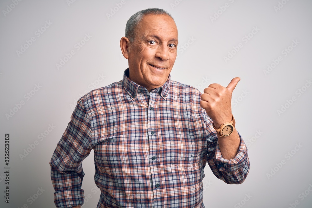 Senior handsome man wearing casual shirt standing over isolated white background smiling with happy face looking and pointing to the side with thumb up. Senior handsome man wearing casual shirt standing over isolated white background smiling with happy face looking and pointing to the side with thumb up.