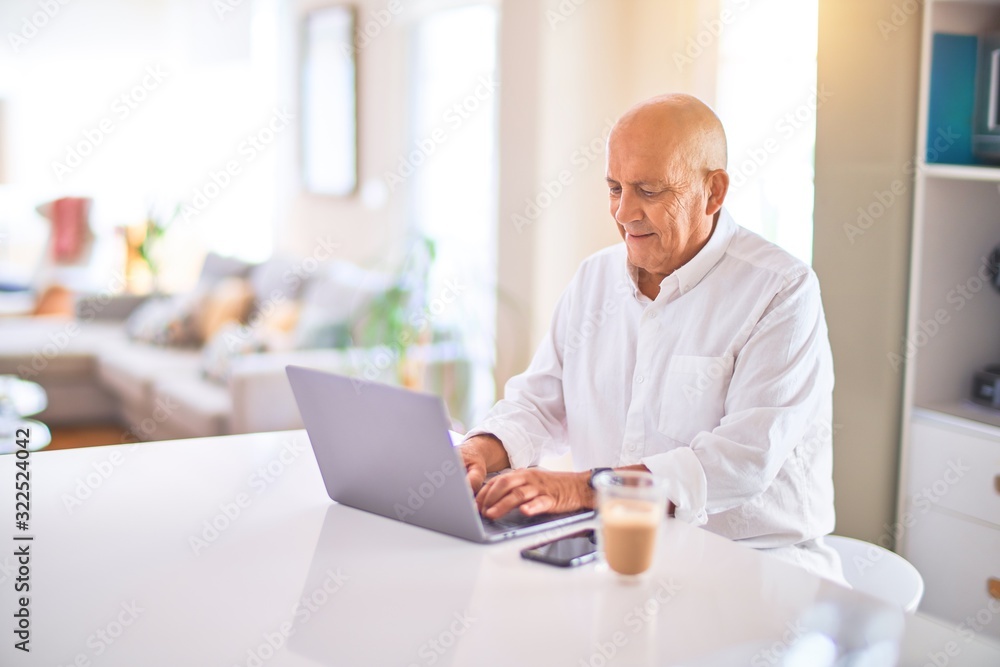 Senior handsome man smiling happy and confident. Sitting using laptop and drinking cup of coffee at home Senior handsome man smiling happy and confident. Sitting using laptop and drinking cup of coffee at home