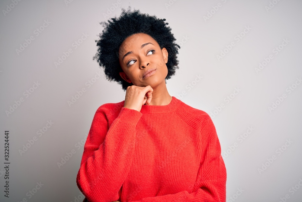 Young beautiful African American afro woman with curly hair wearing red casual sweater with hand on chin thinking about question, pensive expression. Smiling and thoughtful face. Doubt concept. Young beautiful African American afro woman with curly hair wearing red casual sweater with hand on chin thinking about question, pensive expression. Smiling and thoughtful face. Doubt concept.