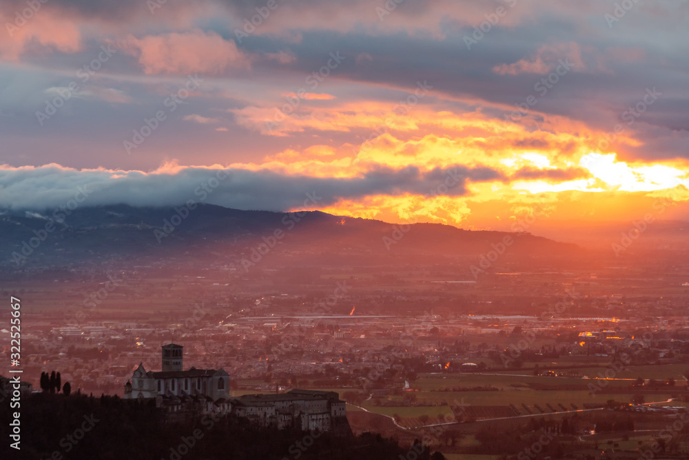 An epic view of St.Francis church in Assisi town (Umbria) with sunrays lighting up half of the valley at sunset