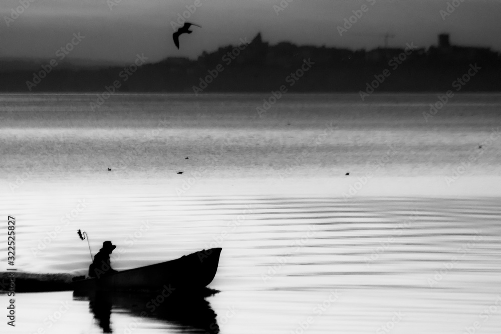 Naklejka premium Trasimeno lake at sunset with a man on a little boat and birds flying