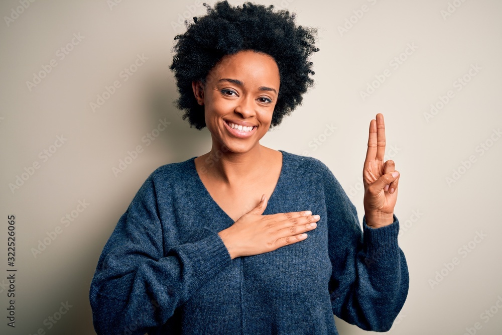 Young beautiful African American afro woman with curly hair wearing casual sweater smiling swearing with hand on chest and fingers up, making a loyalty promise oath Young beautiful African American afro woman with curly hair wearing casual sweater smiling swearing with hand on chest and fingers up, making a loyalty promise oath