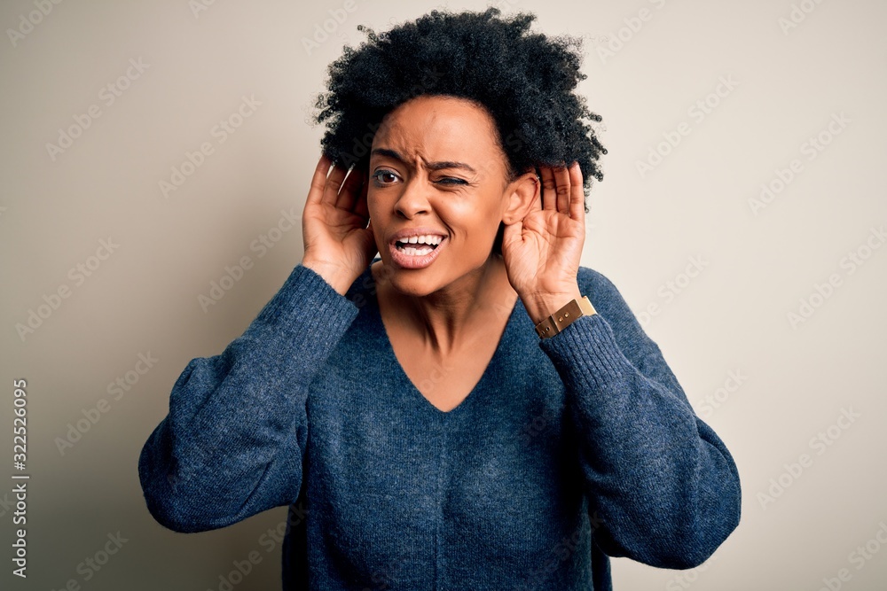 Young beautiful African American afro woman with curly hair wearing casual sweater Trying to hear both hands on ear gesture, curious for gossip. Hearing problem, deaf Young beautiful African American afro woman with curly hair wearing casual sweater Trying to hear both hands on ear gesture, curious for gossip. Hearing problem, deaf