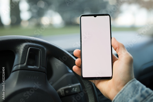 Male hand holding smartphone with blank display in a car at the day 