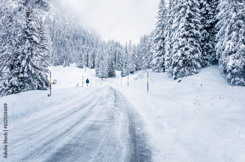 Obraz premium Icy road through a snowy forest in the Alps on a foggy winter day
