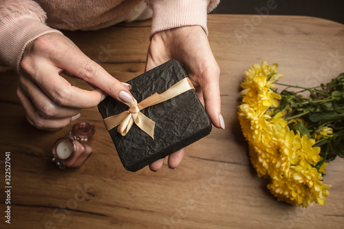  Girl packs a gift. Female hands prepare a gift on a wood background with a yellow flowers. Holiday surprise. Lifestyle.