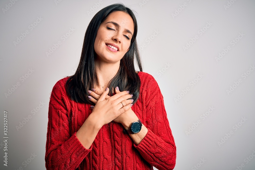 Young brunette woman with blue eyes wearing casual sweater over isolated white background smiling with hands on chest with closed eyes and grateful gesture on face. Health concept. Young brunette woman with blue eyes wearing casual sweater over isolated white background smiling with hands on chest with closed eyes and grateful gesture on face. Health concept.
