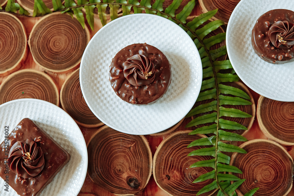 Homemade chocolate snacks with nuts. Dessert with nuts and nougat, covered with chocolate and crushed chocolate flower on a wooden table made of bars. Green fern leaves. Homemade chocolate snacks with nuts. Dessert with nuts and nougat, covered with chocolate and crushed chocolate flower on a wooden table made of bars. Green fern leaves.