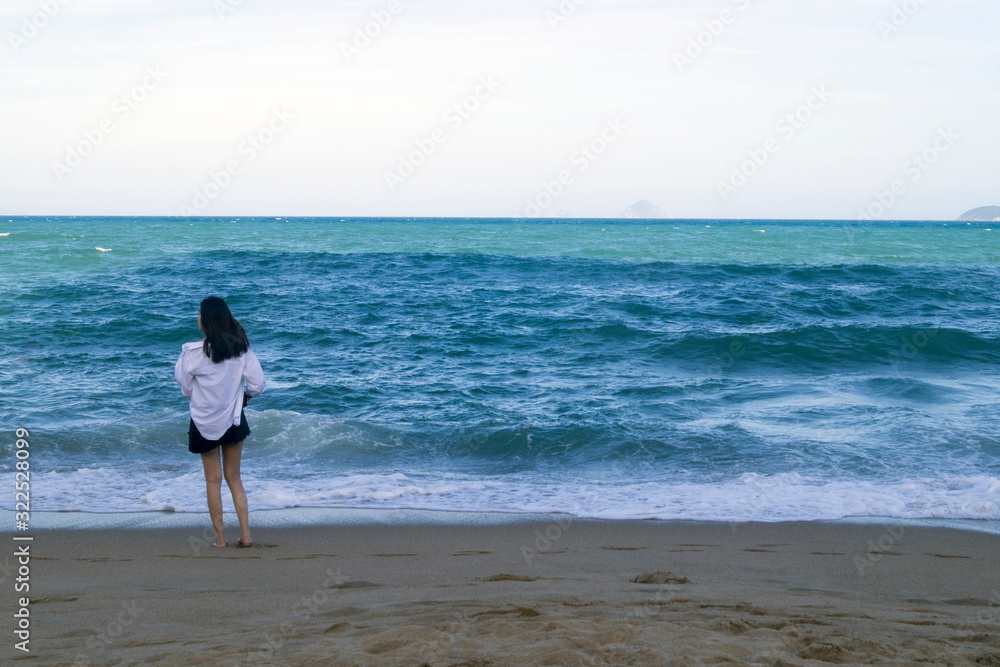 girl with dark hair in a white shirt stands on the seashore