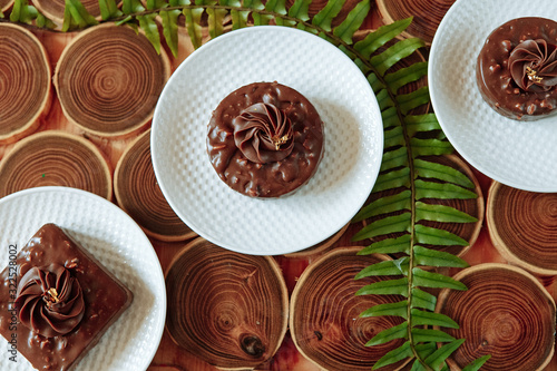 Homemade chocolate snacks with nuts. Dessert with nuts and nougat, covered with chocolate and crushed chocolate flower on a wooden table made of bars. Green fern leaves.