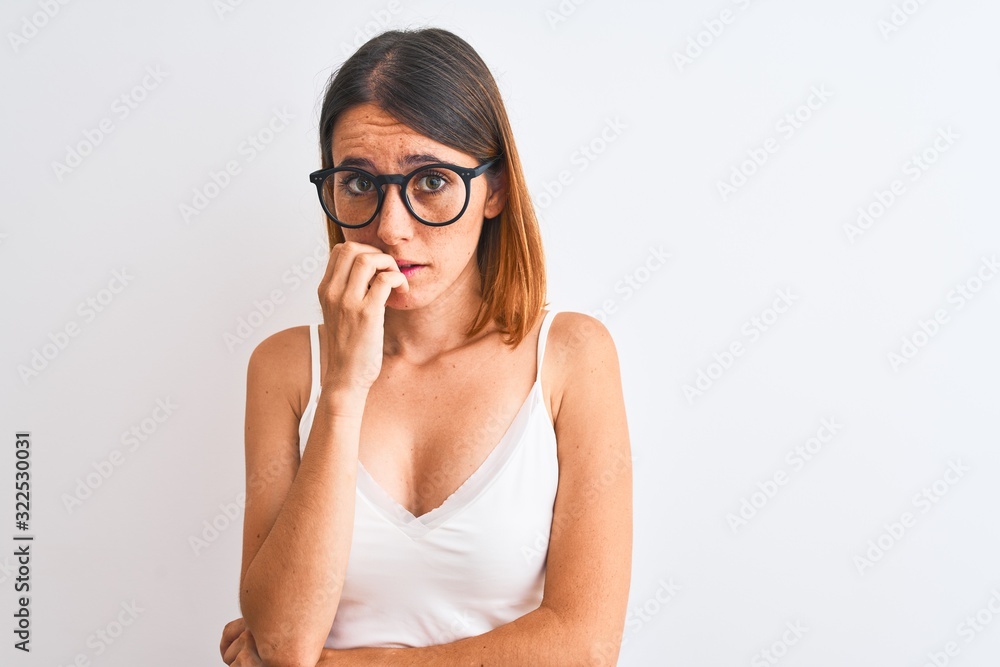 Beautiful redhead woman wearing glasses over isolated background looking stressed and nervous with hands on mouth biting nails. Anxiety problem. Beautiful redhead woman wearing glasses over isolated background looking stressed and nervous with hands on mouth biting nails. Anxiety problem.