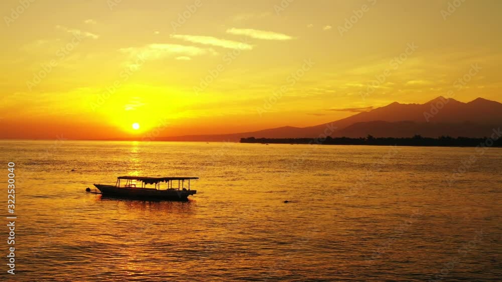 Red and yellow sunset with small fishing boats and mountains in the background across a large body of water Red and yellow sunset with small fishing boats and mountains in the background across a large body of water