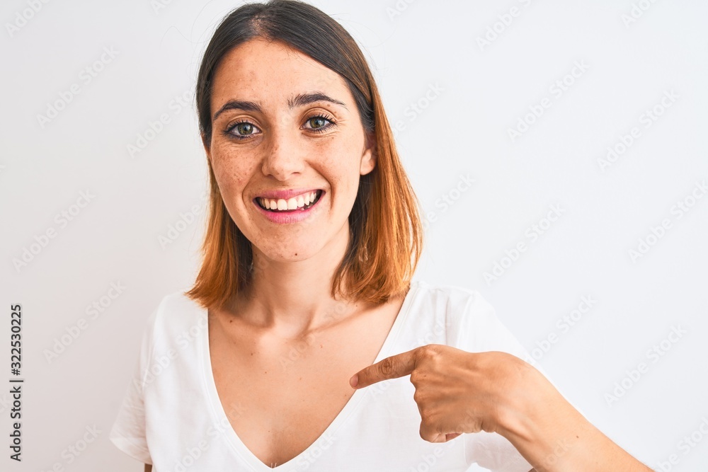 Beautiful redhead woman wearing casual white t-shirt over isolated background with surprise face pointing finger to himself Beautiful redhead woman wearing casual white t-shirt over isolated background with surprise face pointing finger to himself