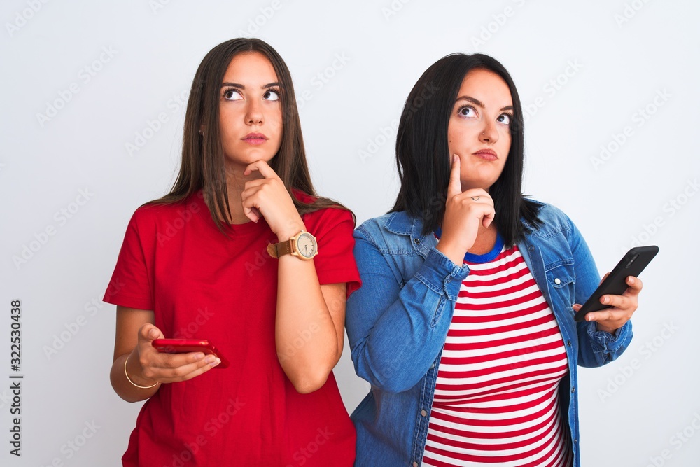 Young beautiful women using smartphone standing over isolated white background serious face thinking about question, very confused idea Young beautiful women using smartphone standing over isolated white background serious face thinking about question, very confused idea