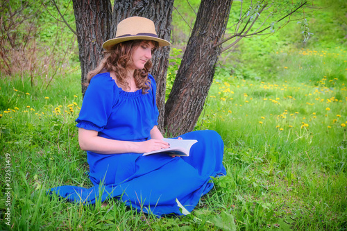 A woman in a straw hat reading a book on the grass sitting under a tree