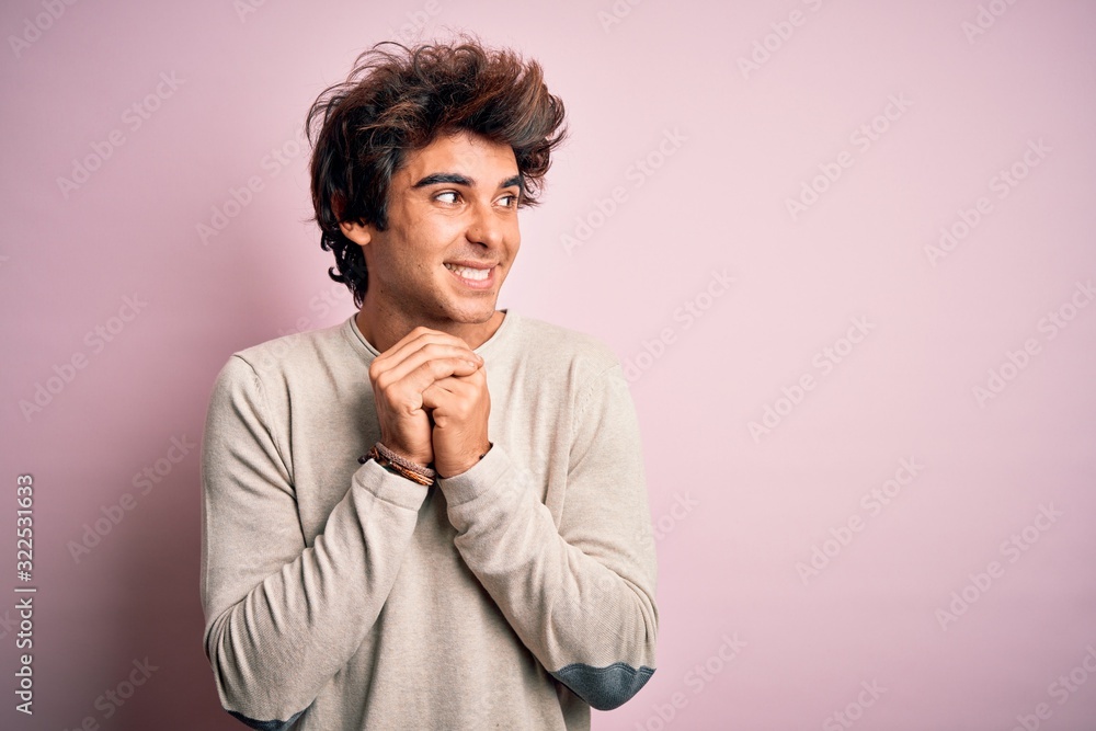 Young handsome man wearing casual t-shirt standing over isolated pink background laughing nervous and excited with hands on chin looking to the side Young handsome man wearing casual t-shirt standing over isolated pink background laughing nervous and excited with hands on chin looking to the side