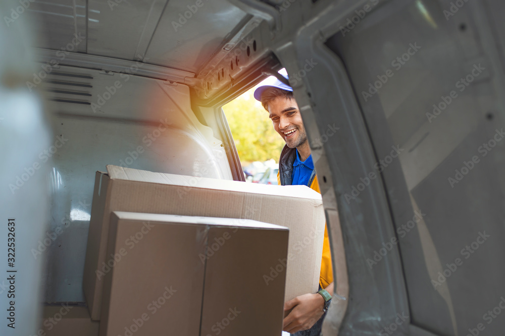 Man loading moving boxes in to his car. View from the car trunk. Close-up Of  Delivery Man Carrying Cardboard Box. Getting his deliveries out. Shot of a courier checking his deliveries in his van
