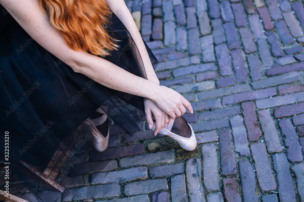 Closeup of ballerina's feet in pointe on street. Strong fit ballerina's legs. Young ballerina woman with red hair in ballet costume dancing and pointe shoes is in beautiful pose dancing on the street. Closeup of ballerina's feet in pointe on street. Strong fit ballerina's legs. Young ballerina woman with red hair in ballet costume dancing and pointe shoes is in beautiful pose dancing on the street.