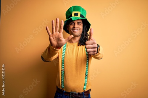 Young african american man wearing green hat celebrating saint patricks day showing and pointing up with fingers number six while smiling confident and happy. © Krakenimages.com