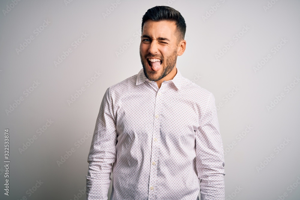 Young handsome man wearing elegant shirt standing over isolated white background sticking tongue out happy with funny expression. Emotion concept. Young handsome man wearing elegant shirt standing over isolated white background sticking tongue out happy with funny expression. Emotion concept.