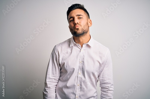 Young handsome man wearing elegant shirt standing over isolated white background looking at the camera blowing a kiss on air being lovely and sexy. Love expression. © Krakenimages.com