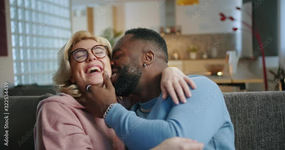 Portrait of romantic couple in love spending amazing time together chilling at home indoor, joyful mixed ethnicity couple enjoying moment of communication talking smiling and laughing on couch Portrait of romantic couple in love spending amazing time together chilling at home indoor, joyful mixed ethnicity couple enjoying moment of communication talking smiling and laughing on couch