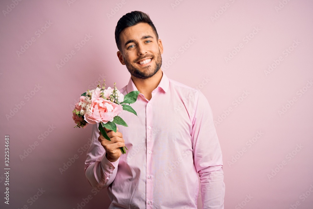 Young romatic man holding bouquet of spring flowers over pink isolatd background with a happy face standing and smiling with a confident smile showing teeth Young romatic man holding bouquet of spring flowers over pink isolatd background with a happy face standing and smiling with a confident smile showing teeth