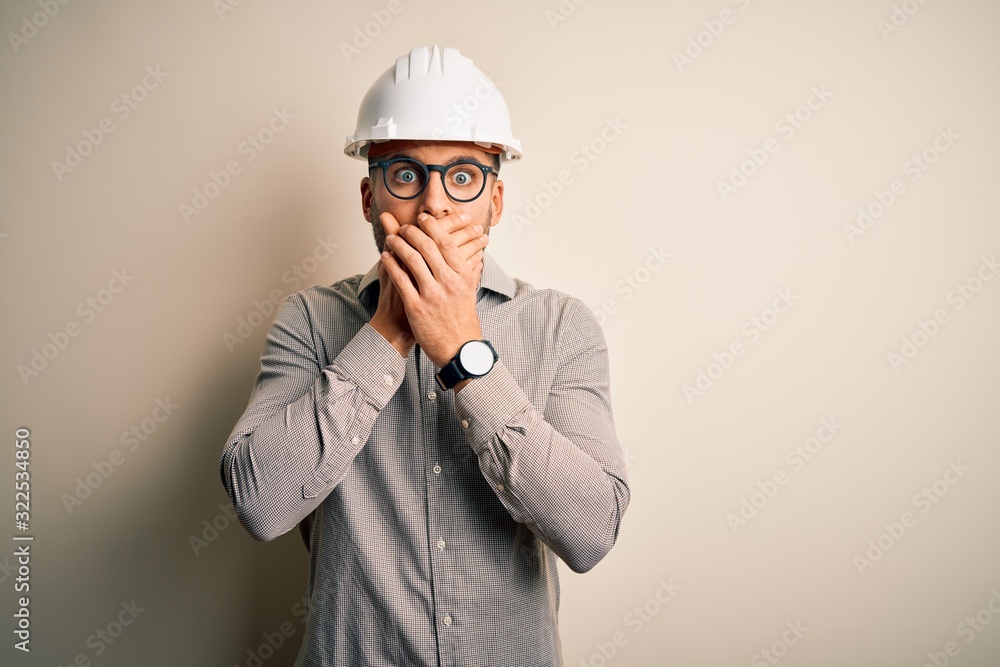 Young architect man wearing builder safety helmet over isolated background shocked covering mouth with hands for mistake. Secret concept. Young architect man wearing builder safety helmet over isolated background shocked covering mouth with hands for mistake. Secret concept.