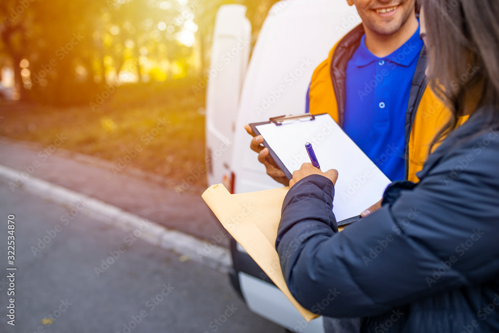 Signing to get her package. Smiling young delivery man holding a delivery package while beautiful young woman putting signature in clipboard. Woman hand accepting a delivery from deliveryman Signing to get her package. Smiling young delivery man holding a delivery package while beautiful young woman putting signature in clipboard. Woman hand accepting a delivery from deliveryman