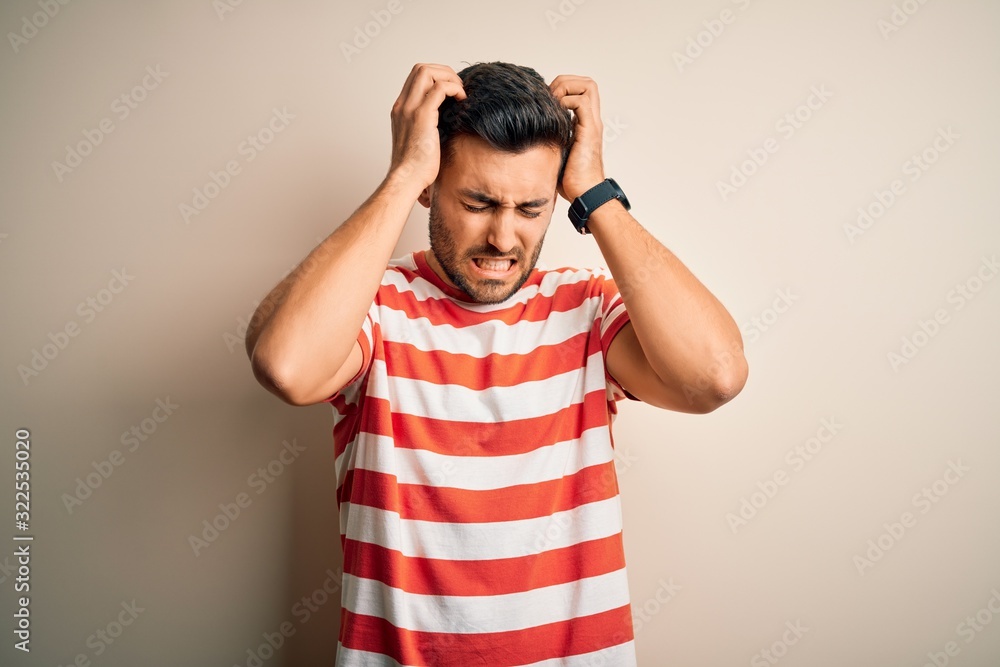 Young handsome man wearing casual striped t-shirt standing over isolated white background suffering from headache desperate and stressed because pain and migraine. Hands on head. Young handsome man wearing casual striped t-shirt standing over isolated white background suffering from headache desperate and stressed because pain and migraine. Hands on head.