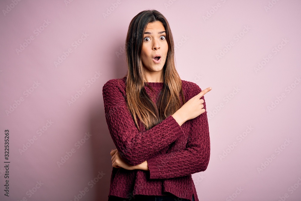 Young beautiful girl wearing casual sweater over isolated pink background Surprised pointing with finger to the side, open mouth amazed expression. Young beautiful girl wearing casual sweater over isolated pink background Surprised pointing with finger to the side, open mouth amazed expression.