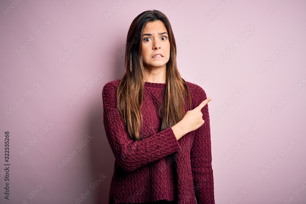 Fototapeta premium Young beautiful girl wearing casual sweater over isolated pink background Pointing aside worried and nervous with forefinger, concerned and surprised expression