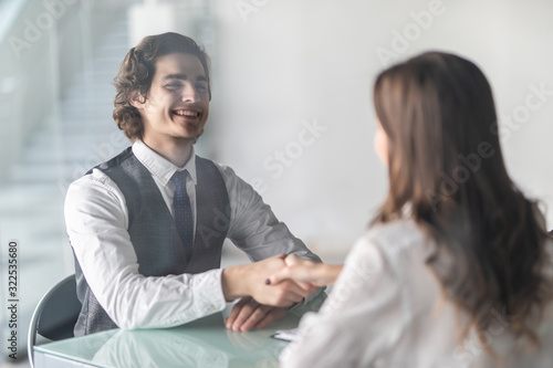 Fototapeta Naklejka Na Ścianę i Meble -  Friendly smiling businessman and businesswoman handshaking over the office desk after pleasant talk and effective negotiation, good relationships. Business concept photo