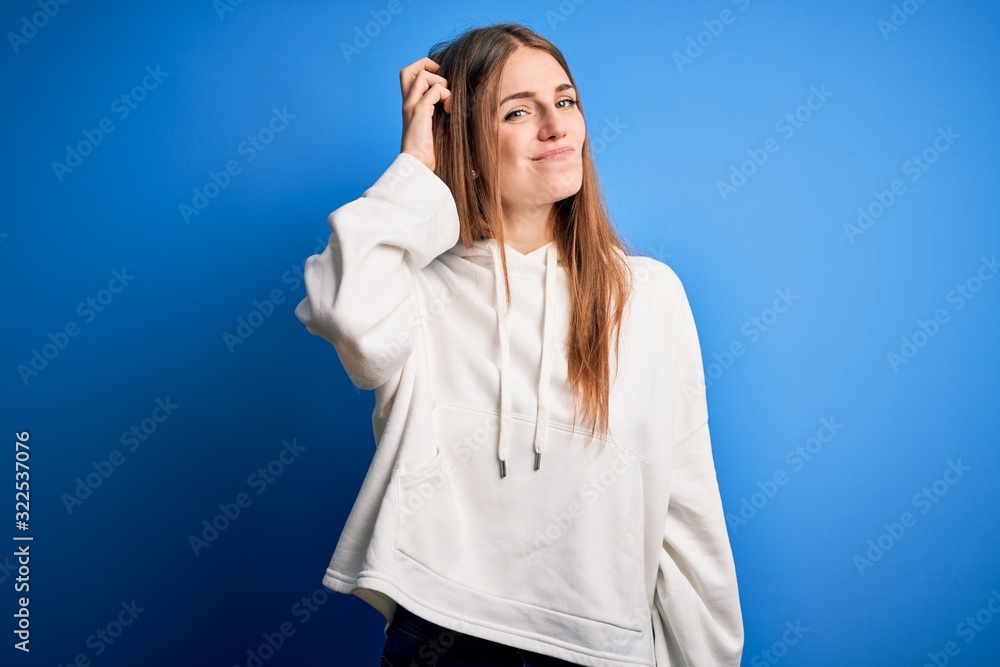 Young beautiful redhead sporty woman wearing sweatshirt over isolated blue background confuse and wonder about question. Uncertain with doubt, thinking with hand on head. Pensive concept. Young beautiful redhead sporty woman wearing sweatshirt over isolated blue background confuse and wonder about question. Uncertain with doubt, thinking with hand on head. Pensive concept.