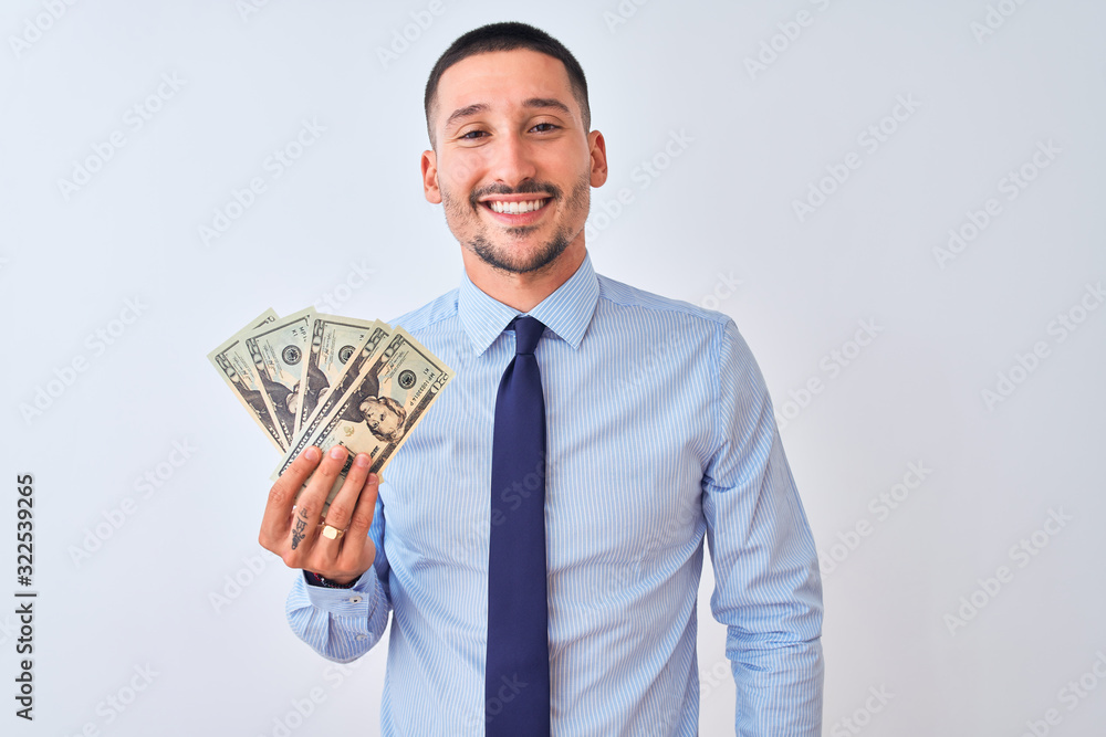 Young handsome business man holding a bunch of bank notes dollars over isolated background with a happy face standing and smiling with a confident smile showing teeth Young handsome business man holding a bunch of bank notes dollars over isolated background with a happy face standing and smiling with a confident smile showing teeth