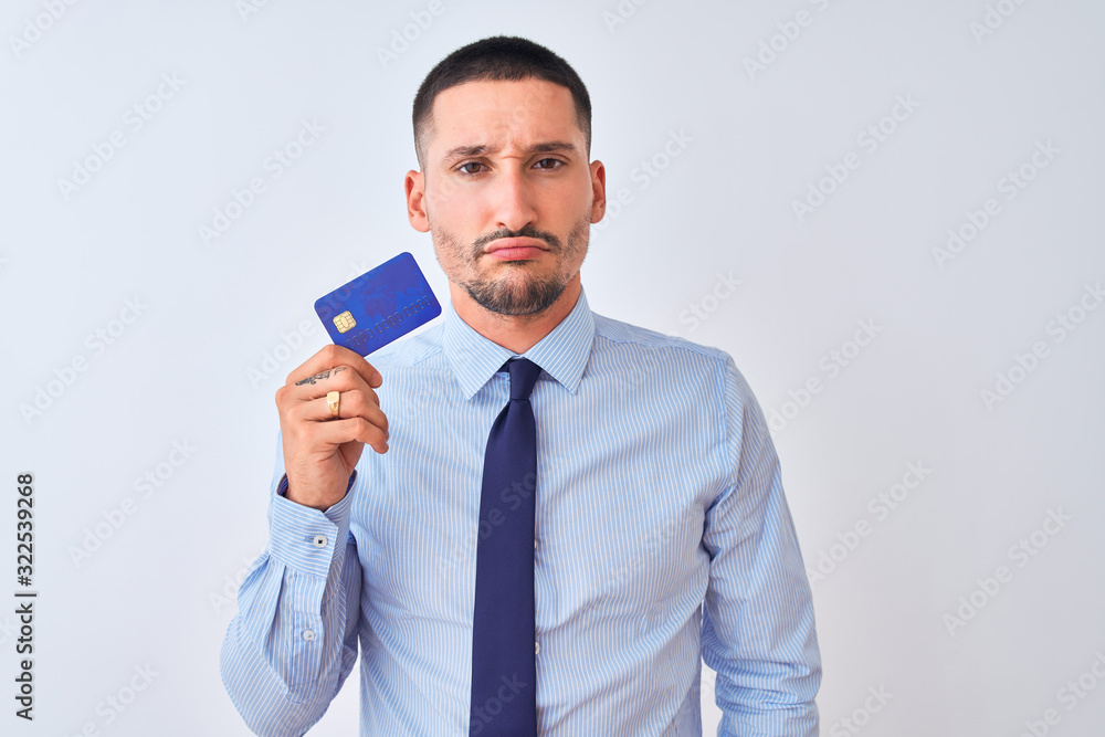Young business man holding credit card over isolated background with a confident expression on smart face thinking serious Young business man holding credit card over isolated background with a confident expression on smart face thinking serious