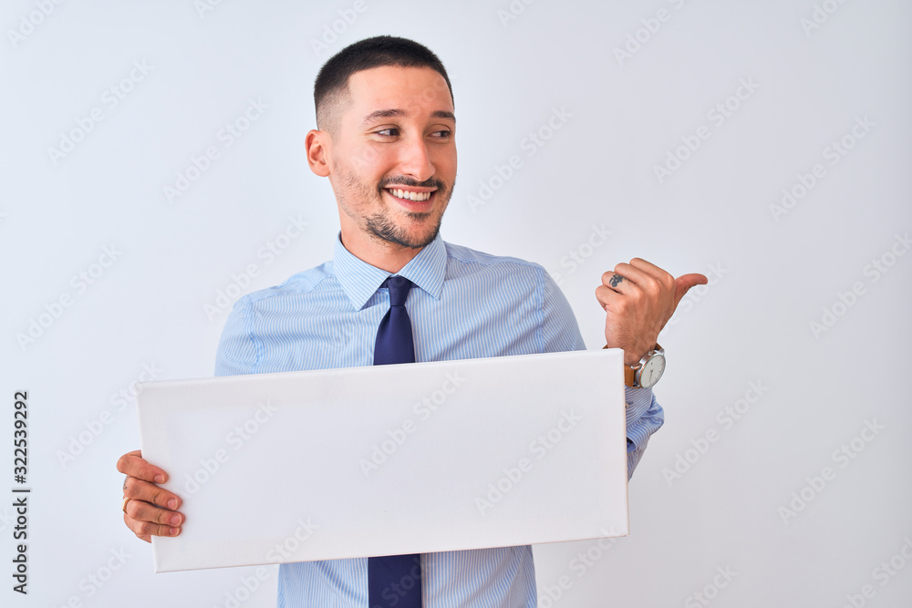 Young business man holding blank banner over isolated background pointing and showing with thumb up to the side with happy face smiling Young business man holding blank banner over isolated background pointing and showing with thumb up to the side with happy face smiling
