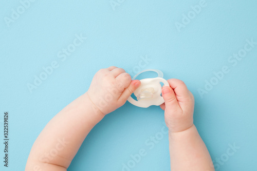 Infant hands holding white soother on light blue floor background. Pastel color. Closeup. First baby toy. Top down view. photo