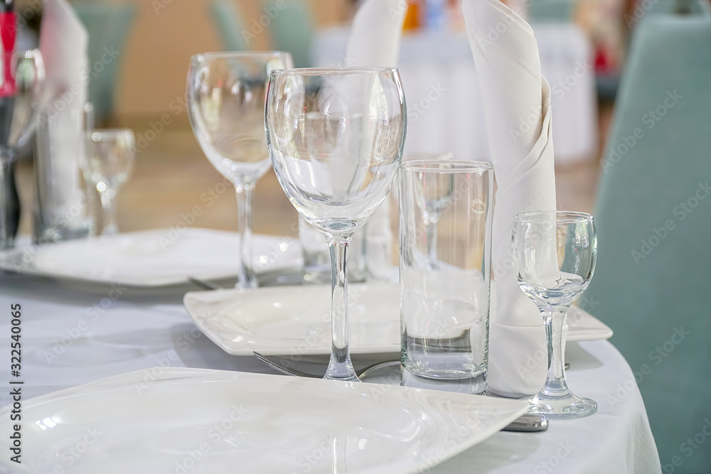 The table in the restaurant is served for dinner. On a table with a white tablecloth, empty wine glasses, a plates, napkins. Selective focus The table in the restaurant is served for dinner. On a table with a white tablecloth, empty wine glasses, a plates, napkins. Selective focus