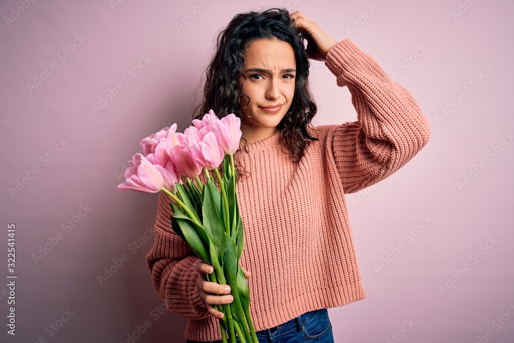 Young beautiful romantic woman with curly hair holding bouquet of pink tulips confuse and wondering about question. Uncertain with doubt, thinking with hand on head. Pensive concept. Young beautiful romantic woman with curly hair holding bouquet of pink tulips confuse and wondering about question. Uncertain with doubt, thinking with hand on head. Pensive concept.