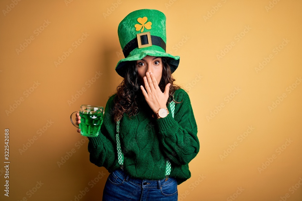 Beautiful curly hair woman wearing hat drinking jar of green beverage on saint patricks day cover mouth with hand shocked with shame for mistake, expression of fear, scared in silence, secret concept Beautiful curly hair woman wearing hat drinking jar of green beverage on saint patricks day cover mouth with hand shocked with shame for mistake, expression of fear, scared in silence, secret concept