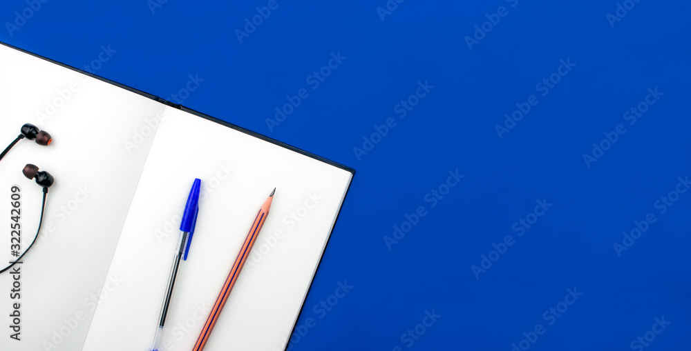School and office supplies flay lay on colorful blue background. Notebook, sketchbook, pen, pencil and headphones top view with copy space. Back to school concept. Web banner template. Stock photo. School and office supplies flay lay on colorful blue background. Notebook, sketchbook, pen, pencil and headphones top view with copy space. Back to school concept. Web banner template. Stock photo.