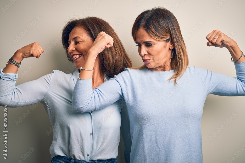 Middle age beautiful couple of sisters standing over isolated white background showing arms muscles smiling proud. Fitness concept.