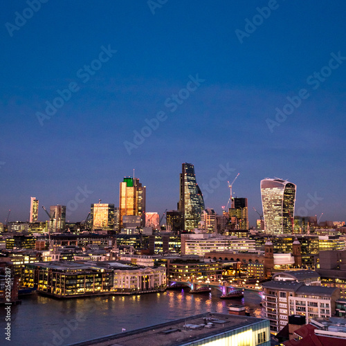 City of London at dusk. An elevated view of the illuminated financial district skyline fronted by the River Thames riverside. © pxl.store