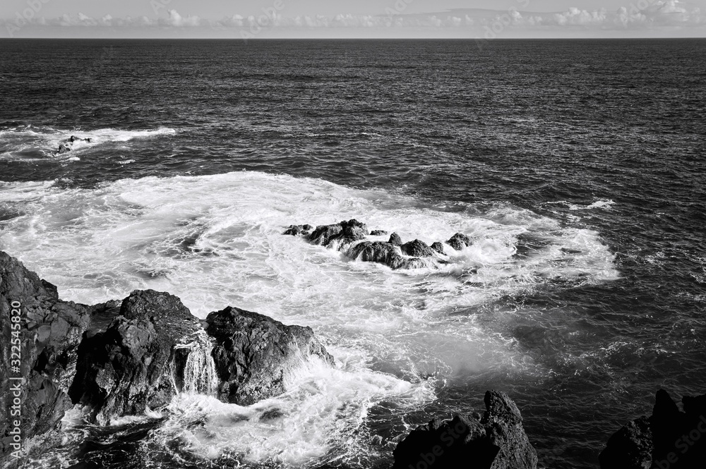 White foam of the waves crashing on the volcanic rock groynes in the Atlantic Ocean (Madeira, Portugal, Europe)