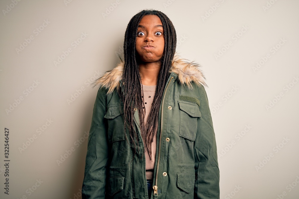 Young african american woman wearing winter parka coat over isolated background puffing cheeks with funny face. Mouth inflated with air, crazy expression. Young african american woman wearing winter parka coat over isolated background puffing cheeks with funny face. Mouth inflated with air, crazy expression.