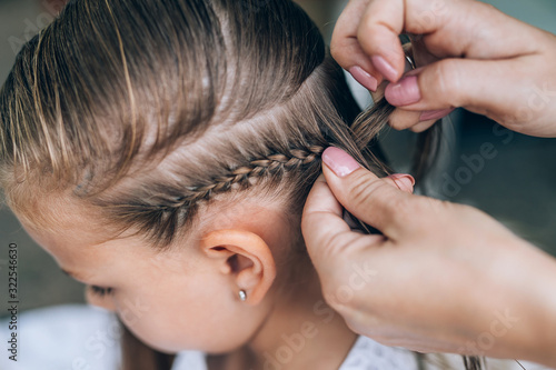 Mother does hair braid to her daughter, close up photo.